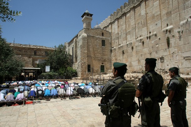Israeli border policemen stand guard as Palestinian men perform the second Friday prayers of the Muslim fasting month of Ramadan outside the Ibrahimi Mosque or the Tomb of the Patriarchs in the West Bank city of Hebron on July 27, 2012. AFP PHOTO / HAZEM BADER        (Photo credit should read HAZEM BADER/AFP/GettyImages)